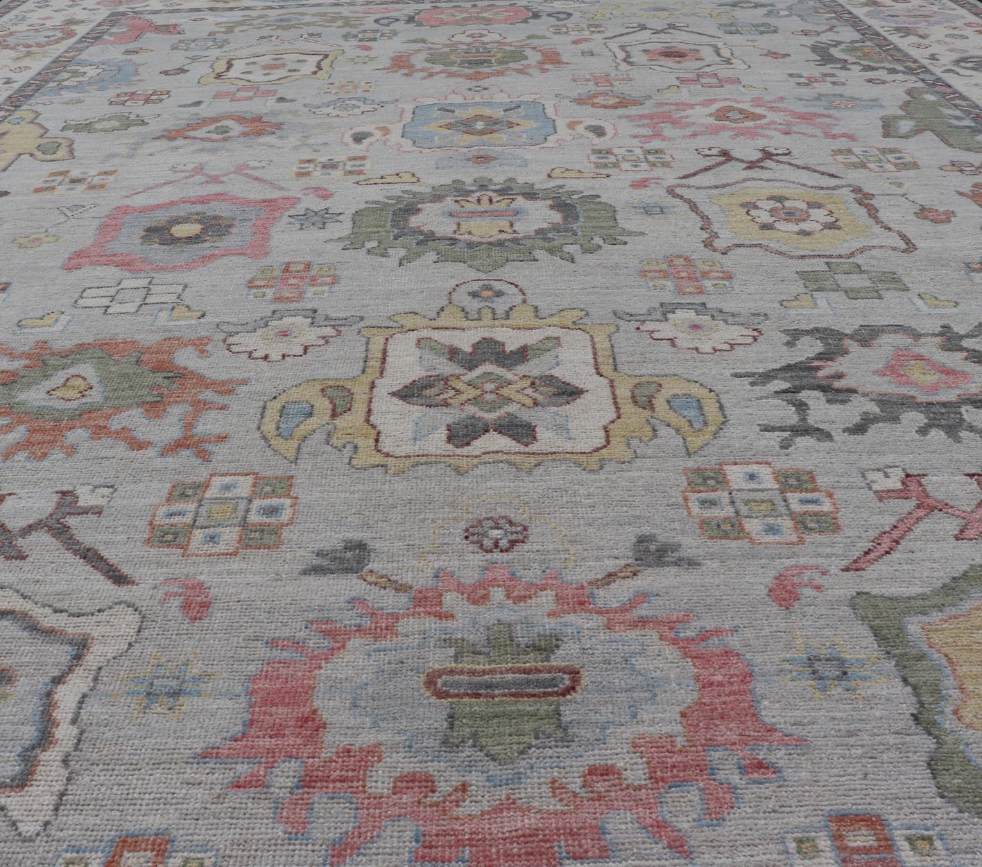 Oushak Floral Motif on Light Grey Background and Colorful Design The border and field are covered in floral - like motifs filled with colors such as pink, green, gold, teal and red - oranges on top of silvery grey background. The border showcases a ... - Keivan Woven ArtsAWR - 6148 - 20025Rug