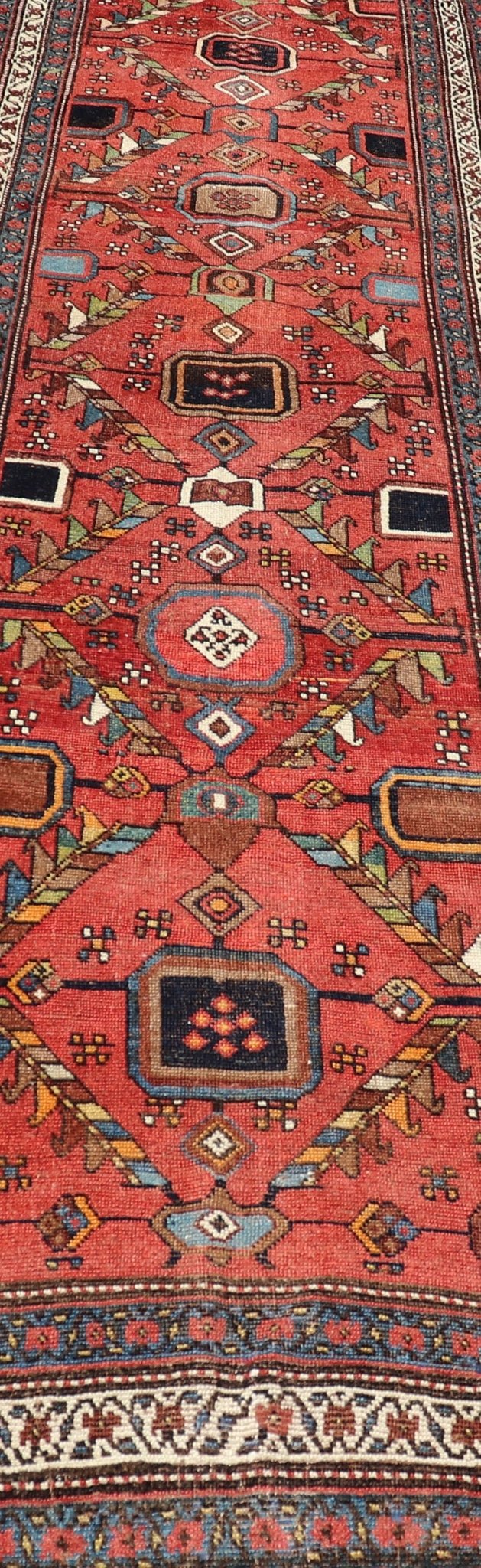 Kurdish Antique Runner in Vibrant Red Background and Multi - tiered Border This early 20th century antique Kurdish runner features a triple - lined floral border, emboldening an ivory stripe between two blue edges. The field features a tribal, sub - g... - Keivan Woven ArtsEMB - 9523 - P13064 - 14668Rug