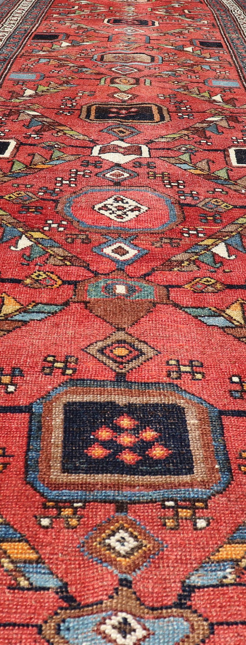 Kurdish Antique Runner in Vibrant Red Background and Multi - tiered Border This early 20th century antique Kurdish runner features a triple - lined floral border, emboldening an ivory stripe between two blue edges. The field features a tribal, sub - g... - Keivan Woven ArtsEMB - 9523 - P13064 - 14668Rug