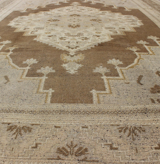 Vintage Turkish Oushak Rug in Brown Background and Neutral Colors Measures: 7'4 x 11'4 This lovely Turkish Oushak from the 1940's features a central medallion, which rests on a dark brown background, is surrounded by a light brown bor... - Keivan Woven ArtsTU - DUR - 506 - 3502