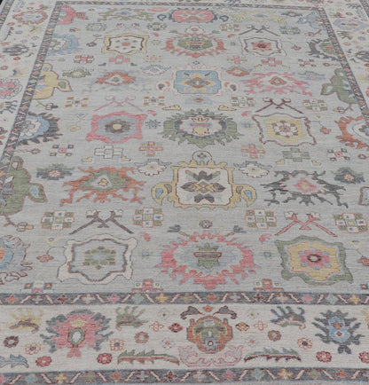 Oushak Floral Motif on Light Grey Background and Colorful Design The border and field are covered in floral - like motifs filled with colors such as pink, green, gold, teal and red - oranges on top of silvery grey background. The border showcases a ... - Keivan Woven ArtsAWR - 6148 - 20025Rug