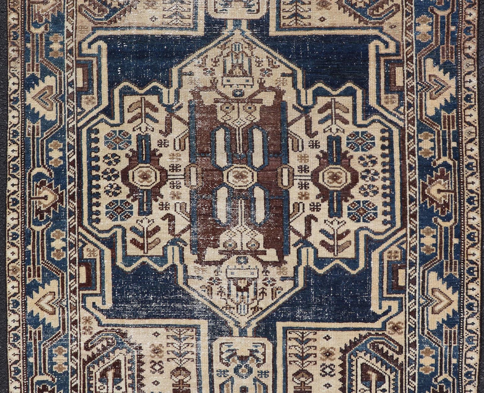 Measures: 4'4 x 6'9 The rug's central field showcases a prominent medallion pattern set against a deep blue background, accented with beige and brown geometric and floral motifs. The medallion itself is highly detailed, featuring a complex arrangem... - Keivan Woven ArtsEMB - 22237 - 22466