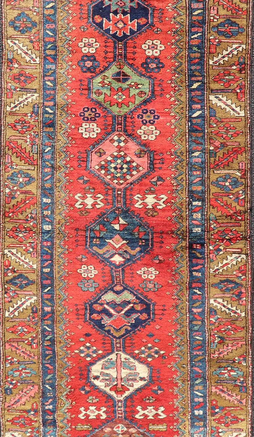 Antique Persian Heriz Runner in Reds, Blues, Pink, Ivory and Earthy Tones This gorgeous antique Persian Heriz runner features a red background imbued with ornate medallions running along the piece. Sub - geometric designs decorate the field, and a... - Keivan Woven ArtsEMB - 9577 - P13510 - 15128Rug