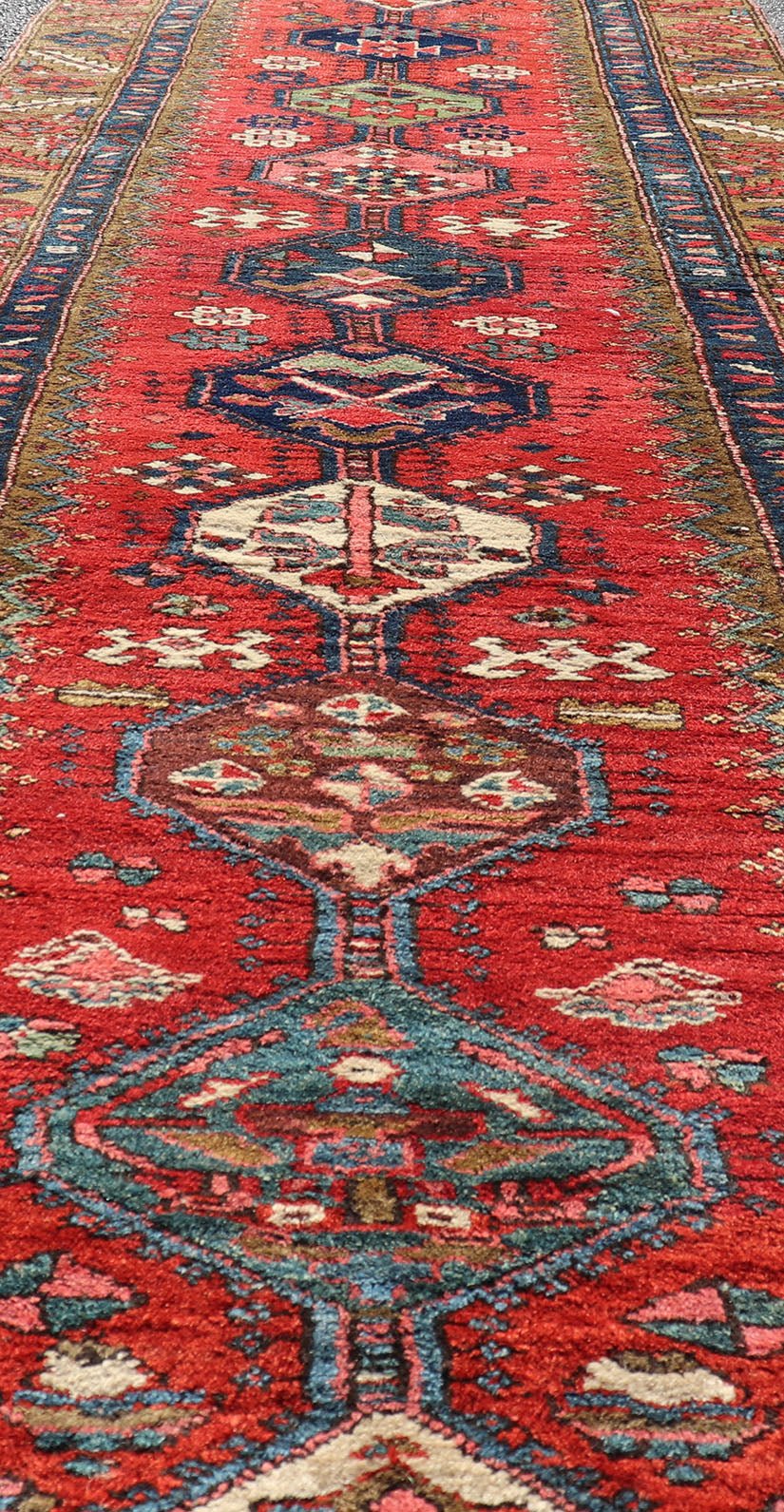 Antique Persian Heriz Runner in Reds, Blues, Pink, Ivory and Earthy Tones This gorgeous antique Persian Heriz runner features a red background imbued with ornate medallions running along the piece. Sub - geometric designs decorate the field, and a... - Keivan Woven ArtsEMB - 9577 - P13510 - 15128Rug