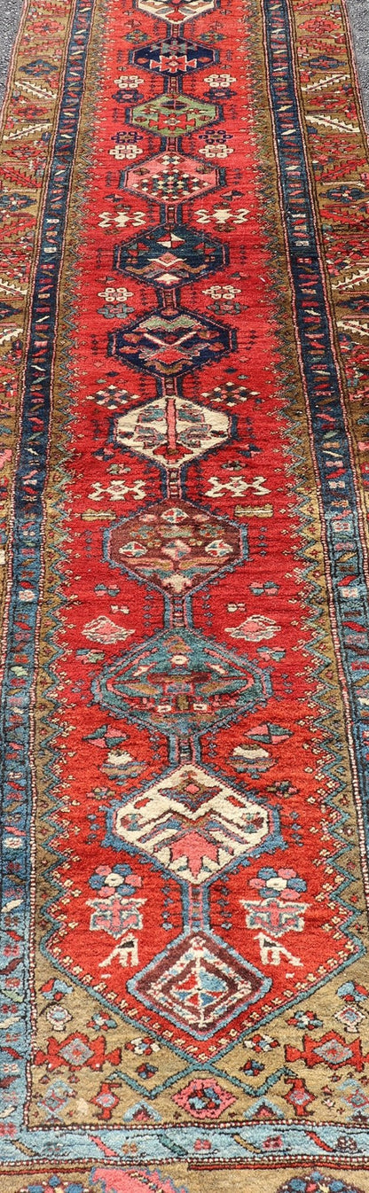 Antique Persian Heriz Runner in Reds, Blues, Pink, Ivory and Earthy Tones This gorgeous antique Persian Heriz runner features a red background imbued with ornate medallions running along the piece. Sub - geometric designs decorate the field, and a... - Keivan Woven ArtsEMB - 9577 - P13510 - 15128Rug