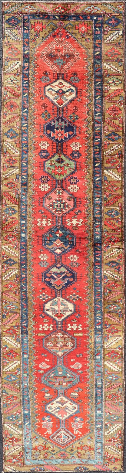 Antique Persian Heriz Runner in Reds, Blues, Pink, Ivory and Earthy Tones This gorgeous antique Persian Heriz runner features a red background imbued with ornate medallions running along the piece. Sub - geometric designs decorate the field, and a... - Keivan Woven ArtsEMB - 9577 - P13510 - 15128Rug