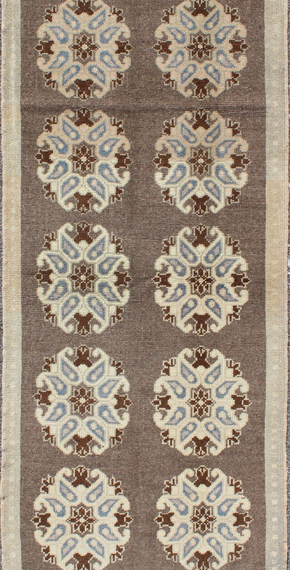 Tribal Turkish Oushak Carpet with Floral Medallions in Taupe, Ivory and Blue Measures: 2'9'' x 6'4''. This Turkish Oushak gallery rug features ten floral medallions that take center stage on a brown field. The border reveals tribal inspiratio... - Keivan Woven ArtsTU - ALK - 3562 - 6787Rug