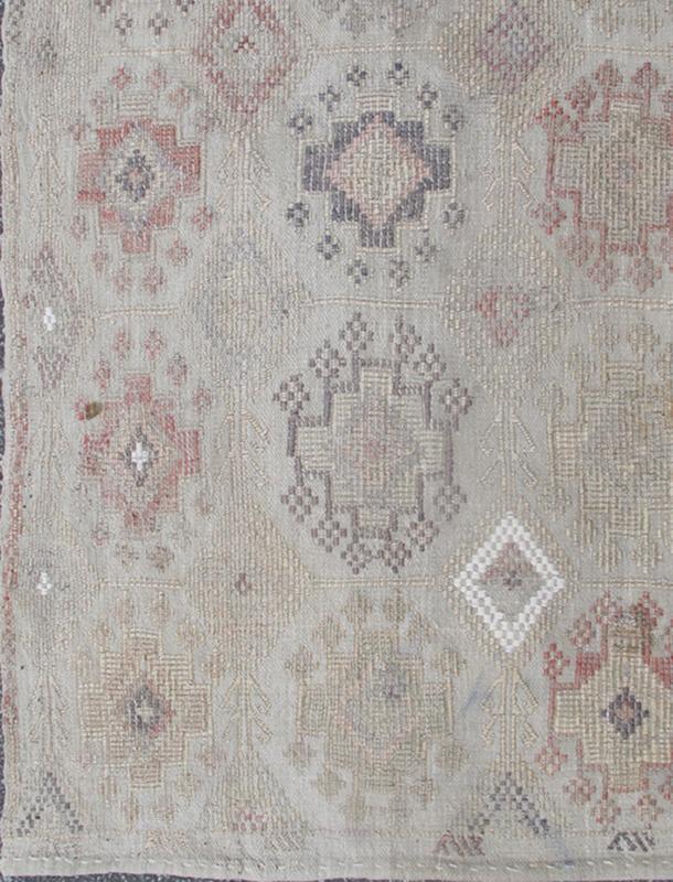Vintage Turkish Kilim Featuring Muted Colors and All - Over Tribal Motif Design Measures 4'7 x 8'0 This rug features an asymmetrical design of tribal crests decorating the light blue - grey field. The crests are rendered in varying muted shades ... - Keivan Woven ArtsTU - NED - 136032 - 4618Rug
