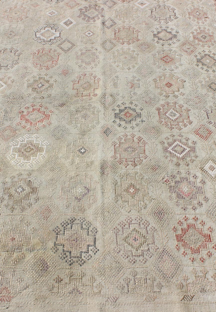 Vintage Turkish Kilim Featuring Muted Colors and All - Over Tribal Motif Design Measures 4'7 x 8'0 This rug features an asymmetrical design of tribal crests decorating the light blue - grey field. The crests are rendered in varying muted shades ... - Keivan Woven ArtsTU - NED - 136032 - 4618Rug